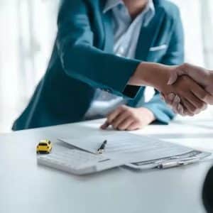 WA-Sales-License-sq - Fusion Business College Two people shake hands over a signed contract on a white desk, with a yellow toy car model and a pen nearby.